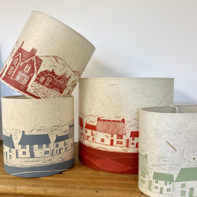 Cottages and houses handprinted onto drum lampshades. Red cottages, blue cottages, green cottages